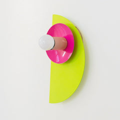 The neon Kin Sconce in chartreuse, doll pink, and orange, featuring a sculptural half-circle backplate and circular shade with a central bulb. This wall sconce channels bold Memphis Group energy with Bauhaus-inspired geometry and saturated color blocking—perfect for playful interiors, maximalist spaces, kids' rooms, or modern art-forward homes that embrace high-impact, unconventional design.