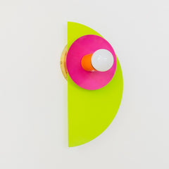 The neon Kin Sconce in chartreuse, doll pink, and orange, featuring a sculptural half-circle backplate and circular shade with a central bulb. This wall sconce channels bold Memphis Group energy with Bauhaus-inspired geometry and saturated color blocking—perfect for playful interiors, maximalist spaces, kids' rooms, or modern art-forward homes that embrace high-impact, unconventional design.