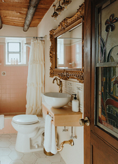 Boho antique style bathroom in a log cabin with stained glass door and peach tile shower with neutral hexagon tile flooring.  Romantic, whimsical, boho, eclectic, and maximalist bathroom design