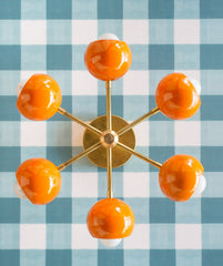 orange and brass midcentury modern style sconce or flushmount style ceiling light.  Great lighting for nurseries or kid related spaced.  Colorful and modern style light fixture. Orange light on a contrasting teal gingham wallpaper.