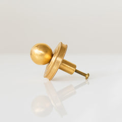 Close-up of the Phillip Drawer Pull, a round solid brass cabinet knob with a 1-inch ball and detailed beaded backplate, installed on a dark wood drawer. Ideal for traditional, transitional, or vintage-inspired kitchens, dressers, and bathroom vanities. A timeless furniture hardware upgrade handcrafted from solid brass with a warm golden finish.