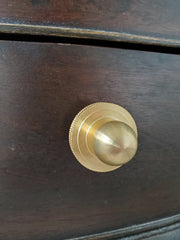Close-up of the Phillip Drawer Pull, a round solid brass cabinet knob with a 1-inch ball and detailed beaded backplate, installed on a dark wood drawer. Ideal for traditional, transitional, or vintage-inspired kitchens, dressers, and bathroom vanities. A timeless furniture hardware upgrade handcrafted from solid brass with a warm golden finish.
