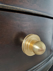Close-up of the Phillip Drawer Pull, a round solid brass cabinet knob with a 1-inch ball and detailed beaded backplate, installed on a dark wood drawer. Ideal for traditional, transitional, or vintage-inspired kitchens, dressers, and bathroom vanities. A timeless furniture hardware upgrade handcrafted from solid brass with a warm golden finish.