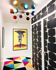 Prism Chandelier in a playful hallway with bold black and white graphic wallpaper, Batman comic art poster, and colorful geometric rug. A mid-century modern rainbow sputnik ceiling light adds dopamine décor energy and eclectic style to this fun modern home interior.