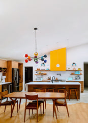 Prism Chandelier over a mid-century modern dining table in an open kitchen with walnut cabinets, yellow accent hood, and eclectic pendant lights. A rainbow sputnik ceiling fixture with brass arms adds dopamine décor style and vibrant personality to this colorful modern home.