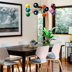 Prism Chandelier hanging over a modern wood dining table with white mid-century style chairs and large black-and-white wall art. A rainbow sputnik ceiling light with brass frame brings eclectic décor, dopamine design energy, and bold mid-century modern style to the dining space.
