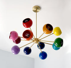 Close-up view of the Prism Chandelier with 12 colorful powder-coated shades in red, pink, orange, yellow, green, blue, and purple on a sleek brass sputnik frame. A mid-century modern rainbow ceiling light fixture that brings dopamine décor, eclectic energy, and bold style to dining rooms, playrooms, nurseries, and modern living spaces.