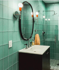 Orange and Chrome Camp sconces in a green subway tile bathroom