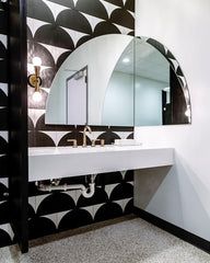 Modern Graphic black and white arch tile with a dramatic arch mirror in a commercial bathroom.  Features a geometric small Constance sconce by Sazerac Stitches in black and brass.  Art deco inspired black and white bathroom