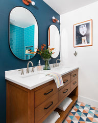 teal bathroom with terra cotta colored sconces, a wood vanity, and a geometric tile floor