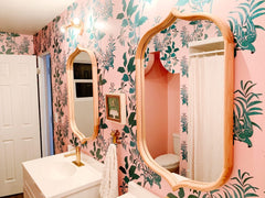 pink and green wallpapered bathroom with brass sconces