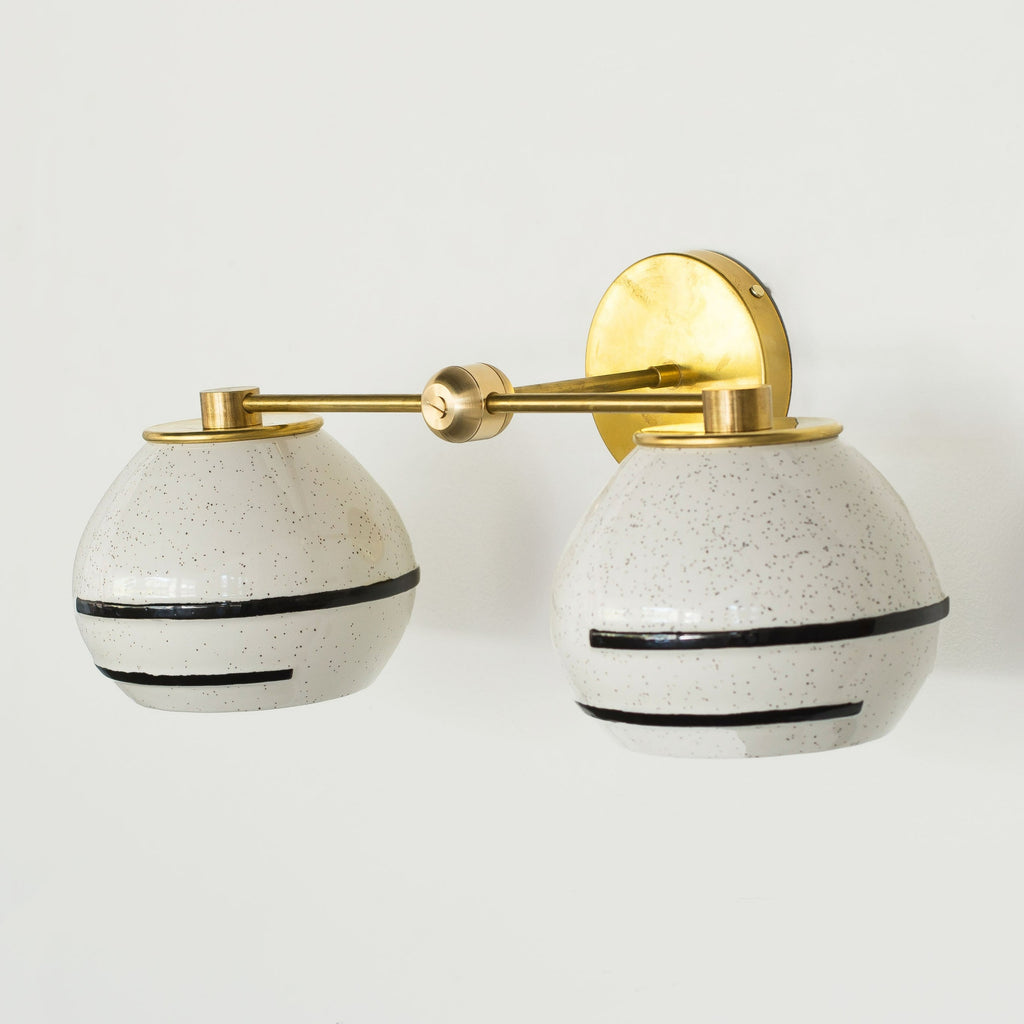 Organic modern two light wall sconce with speckled ceramic shades that have an accent line around the perimeter