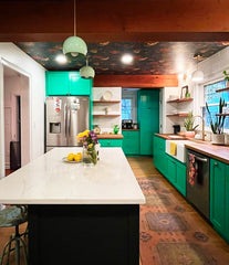 Rustic kitchen with green cabinets, large marble island, wood beams, and mint and brass pendant lights.  Ceiling wallpapered with a moody floral print
