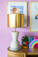 Colorful art gallery on pastel purple walls with a natural wood credenza and cream and brass table lamps