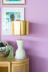 Colorful art gallery on pastel purple walls with a natural wood credenza and cream and brass table lamps