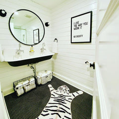 Black and white farmhouse style bathroom with tiger rug, shiplap, and black floral sconces