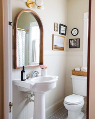 traditional style bathroom in neutral colors with a wood mirror, eclectic frames, and modern brass and white wall sconce by sazerac stitches