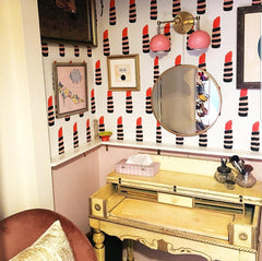Pink and brass two light wall sconce above a makeup vanity space. Features lipstick wallpaper, a girly vintage desk, and pink wainscotting.  Very feminine.