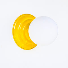 Yellow flushmount ceiling light or wall sconce with a frosted white globe. Stepping back into a bygone era with a touch of modern minimalism, the Abeille Sconce or Flushmount is an artistic blend of form and function. This wall sconce doubles as a flushmount ceiling light, making it a versatile lighting solution for any space. Designed akin to a beehive, its charismatic shape is complemented by curated color options that add a playful element to its retro appeal.
