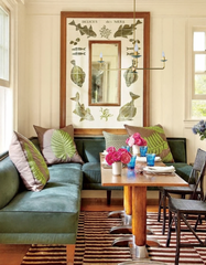 Adele Chandelier in brass with olive green scalloped details, suspended over a warm wood dining table with built-in green velvet banquette seating and botanical wall art. This modern-meets-retro chandelier enhances breakfast nooks and dining spaces with soft, romantic light and customizable color options. A versatile statement chandelier for transitional and eclectic home interiors.