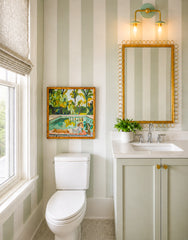 The Adele Two Light Sconce in mint and brass adds just the right touch of softness to this light, neutral bathroom. Shown above a gold-framed mirror in a striped powder room with pale green walls, a matching vanity, and crisp white finishes, it brings a subtle feminine feel without being overly sweet. This is the kind of bathroom sconce that works beautifully in modern homes that still want warmth, charm, and personality. The clean lines keep it fresh, while the mint and brass palette gives it a polished, s