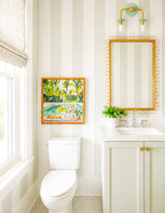 The Adele Two Light Sconce in mint and brass adds just the right touch of softness to this light, neutral bathroom. Shown above a gold-framed mirror in a striped powder room with pale green walls, a matching vanity, and crisp white finishes, it brings a subtle feminine feel without being overly sweet. This is the kind of bathroom sconce that works beautifully in modern homes that still want warmth, charm, and personality. The clean lines keep it fresh, while the mint and brass palette gives it a polished, s