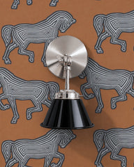 A black wall sconce with a glossy cone shade and polished nickel hardware. A swivel knuckle with a wing nut on the round backplate lets you tilt the shade. It hangs on rust orange wallpaper printed with bold gray and black line drawn horses. Mount it by a bed, in a study, or beside a mirror as a vanity light. Black and silver look sharp against the warm rust, giving it a graphic, equestrian, slightly 70s feel that suits dens, home offices, and eclectic modern rooms.