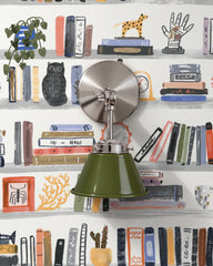An olive green wall sconce with a glossy cone shade and polished nickel hardware. A swivel knuckle with a wing nut on the round backplate lets you tilt the shade. It sits on hand painted bookshelf wallpaper full of colorful books, a black owl, trailing plants, and quirky curios. Tilt it down as a reading light beside a chair or bed. Olive and silver suit a home library, a study, or a kids reading nook, and fit eclectic, bookish, and playful modern decor.