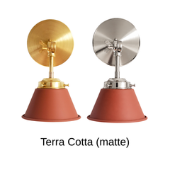 A terracotta wall sconce with a matte cone shade, shown in Terra Cotta with brass or nickel hardware. It has a single light, a round backplate, and a swivel knuckle with a wing nut so you can tilt the shade toward a bed, a mirror, or a sink. Hang one by a bed, a pair beside a bathroom mirror as a vanity light, or one over a kitchen counter. Matte clay red sits well with sage or cream plaster walls, zellige tile, and linen, so it suits Mediterranean, desert modern, and earthy boho rooms.