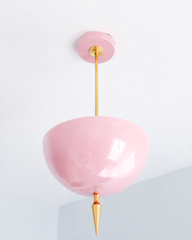 Blush pink pendant light with a brass spike finial, the Alexander Pendant sends light up instead of down, so the glossy pink dome bounces a soft, romantic glow off the ceiling. That uplight pendant design paired with the oversized art deco spike gives the sweetness a hard architectural edge instead of letting it go too soft. Statement girls room pendant, nursery ceiling light, or grandmillennial dining room fixture for maximalist decor that wants real presence overhead without losing its feminine charm.