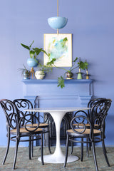 The Alexander pendant in pastel celestial blue and brass pops against a deep blue wall and mantel styling, with layered greenery, sculptural objects, and a framed abstract print. This steel dome pendant is all about mood lighting, washing light up toward the ceiling for an atmospheric glow. Clean, masculine shape with a  brass spike detail for a modern classic look that works in eclectic interiors, maximalist spaces, and color-forward dining nooks or breakfast corners that do not need a ton of direct light.