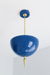 Handmade blue pendant light in a soft, glossy denim tone that works like a colorful neutral — a high-gloss powder-coated dome in dusty chambray blue, lifted by a slim brass stem and a hand-turned brass finial. The color is easygoing and versatile: it reads faded workwear-blue in daylight and mellows under lamplight, so it layers into a room as naturally as your favorite pair of jeans, playing well with brass, wood, white, and warm neutrals. Perfect over a kitchen island, mudroom, breakfast nook, or entryway