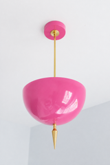 Handmade pink pendant light in a bold, glossy doll pink — a high-gloss powder-coated dome in vivid bubblegum, lifted by a slim brass stem and a hand-turned brass finial. The color is playful and saturated: it reads bright candy-pink in daylight and glows warmer under lamplight, so it brings joyful, feminine energy against warm brass, white walls, natural wood, or a color-drenched backdrop. Perfect over a kitchen island, a vanity, a girl's room, a dressing room, or an entryway that could use a hit of fun. Sh