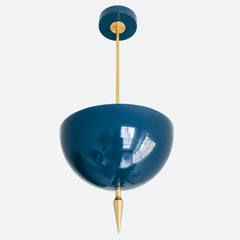 Handmade lagoon pendant light in a rich jewel-toned blue-green — a high-gloss powder-coated dome poised between teal and navy, grounded by a slim brass stem and a hand-turned brass finial. The saturated color reads slate-blue in daylight and deepens to an inky peacock tone under lamplight, so it works like a jewel-toned neutral against warm wood, white walls, or patterned wallpaper. Perfect over a kitchen island, powder room, or entryway that needs a hit of depth. Shop handmade blue pendant lighting, glossy