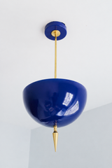 Handmade navy pendant light in a deep, glossy blue that works like a dressed-up neutral — a high-gloss powder-coated dome in rich ink-navy, lifted by a slim brass stem and a hand-turned brass finial. The color is classic and saturated: it reads true navy in daylight and turns nearly midnight under lamplight, so it brings a tailored, timeless depth against warm brass, white walls, natural wood, or a moody backdrop. Perfect over a kitchen island, a study, a dining area, or an entryway that could use a grounde