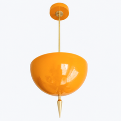 Alexander Pendant in glossy marigold-orange powder-coat, shown at a three-quarter angle with light pooling across the domed metal shade, slim brass stem, and turned brass finial spike below.