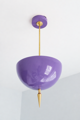 Handmade orchid pendant light that turns purple into a grown-up neutral — a high-gloss powder-coated dome in soft violet, warmed by a slim brass stem and a hand-turned brass finial that drops to a point. The color is saturated but never loud: it reads lavender in daylight and deepens toward amethyst under lamplight, making it easy to layer into a room you already love. Perfect over a kitchen island, in an entryway, or as a jewel-toned accent in a powder room or reading nook. Shop handmade purple pendant lig