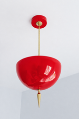 Handmade red pendant light in a bold, glossy true red — a high-gloss powder-coated dome in vivid lacquer-red, lifted by a slim brass stem and a hand-turned brass finial. The color is confident and saturated: it reads bright cherry in daylight and glows deeper, almost lipstick-red, under lamplight, so it makes an unapologetic statement against warm brass, white walls, natural wood, or a moody dark palette. Perfect over a kitchen island, a bar nook, a dining area, or an entryway that could use a jolt of drama