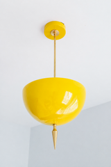 Handmade yellow pendant light in a punchy high-gloss finish that reads pure sunshine — a powder-coated dome in saturated primary yellow, lifted by a slim brass stem and a hand-turned brass finial that drops to a fine point. The color is bright and glossy without tipping into neon: it bounces light in the daytime and glows lemon-warm under bulbs, making it the kind of joyful accent that anchors a color-drenched room or wakes up an all-white one. Perfect over a kitchen island, a breakfast nook, a kid's room, 