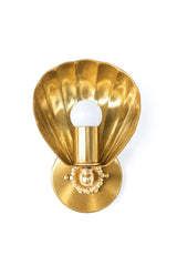 The Coquille Sconce in all brass: a single-light wall sconce with a fluted scallop shell shade that cups the bulb, set on a round brass backplate with a rosette and ball detail. The shell throws warm light back onto the wall. Use a pair as vanity lights on either side of a bathroom mirror, or as a hallway or bedside sconce. Fits coastal, art deco, Hollywood Regency, and grandmillennial rooms, and works with any wall color. Handmade in New Orleans.