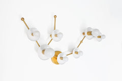 Horizontal view of the White Aquarius star sign wall sconce in brass with multiple white powder coated steel discs and globe bulbs, a constellation style astrology lighting fixture that works as a statement bathroom vanity light for maximalist design lovers and mid century modern decor.