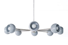 Arcenciel chandelier in slate grey with glossy globe shades on sleek chrome arms and center hub, a modern sputnik-style statement ceiling light photographed against a white brick wall, perfect for mid century modern interiors, minimalist design homes, and contemporary spaces needing a sculptural chandelier for a dining room, living room, or modern entryway.