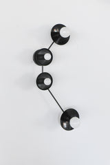 Aries zodiac constellation light fixture in all black metal with four round disc shades and white globe bulbs, modern sculptural wall sconce inspired by star signs, graphic mid century modern style lighting for hallway, entryway, bedroom, above nightstands, or moody bathroom vanity, minimalist black wall lighting for modern farmhouse, contemporary, maximalist, and eclectic interior design