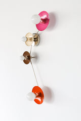 Colorblocked Aries wall sconce with four round saucer disc shades in doll pink, cream, fudge brown, and flame orange, connected by sleek chrome arms with white globe bulbs, photographed on a clean white background. Sculptural modern lighting for a pretty powder room, feminine bathroom vanity, eclectic bedroom, colorful hallway, mid century modern living room, or playful kids room, an instant pop of color for maximalist and modern decor.