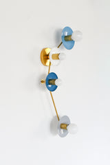 Colorblocked Aries wall sconce with four round saucer disc shades in hydrangea blue, white, denim blue, and slate grey, paired with warm brass arms and white globe bulbs on a clean white background. Sculptural modern lighting with a mid century modern vibe for a bathroom vanity, pretty powder room, hallway, bedroom, entryway, or kids room. Great for coastal decor, Scandinavian style interiors, eclectic color-forward homes, and designer lighting projects.
