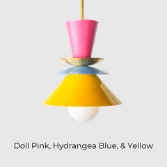 The Astro Pendant light by Sazerac Stitches, featuring a playful stacked design with bold enamel-coated metal shades in Doll Pink, Chrome or Brass, Hydrangea Blue, and Yellow. The geometric composition creates a striking visual contrast, suspended from a sleek rod with an exposed bulb for a modern touch.