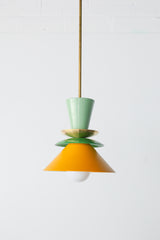 Colorblocked Astro Pendant light with a modern geometric silhouette, featuring powdercoated aluminum shades in Vista Green, Spring Green, and Matte Mustard. Topped with a brass accent and suspended from a brass rod. Handcrafted in New Orleans by Sazerac Stitches, this statement pendant is ideal for kitchens, dining rooms, or bold interior spaces with a playful or maximalist design aesthetic.