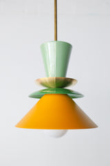 Colorblocked Astro Pendant light with a modern geometric silhouette, featuring powdercoated aluminum shades in Vista Green, Spring Green, and Matte Mustard. Topped with a brass accent and suspended from a brass rod. Handcrafted in New Orleans by Sazerac Stitches, this statement pendant is ideal for kitchens, dining rooms, or bold interior spaces with a playful or maximalist design aesthetic.