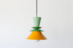 Colorblocked Astro Pendant light with a modern geometric silhouette, featuring powdercoated aluminum shades in Vista Green, Spring Green, and Matte Mustard. Topped with a brass accent and suspended from a brass rod. Handcrafted in New Orleans by Sazerac Stitches, this statement pendant is ideal for kitchens, dining rooms, or bold interior spaces with a playful or maximalist design aesthetic.
