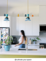 Pair of modern mid century pendant lights in teal blue with brass accents hanging over a bright white kitchen island, colorful contemporary kitchen lighting with layered cone shades and sculptural silhouette, statement pendant fixtures for a modern kitchen remodel, retro inspired island lighting for eclectic, maximalist, and design forward homes, stylish brass and teal ceiling pendants above a minimalist white cabinet kitchen